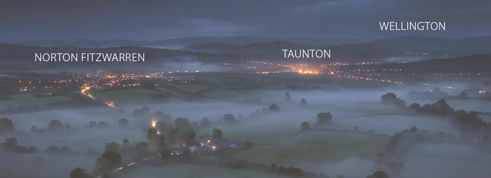 The Somerset countryside at dusk, with the lights of Norton Fitzwarren, Taunton and Wellington in the valley below.
